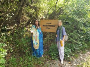 Two women standing next to a sign in the woods.