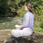 A woman sitting on the ground in front of a river.