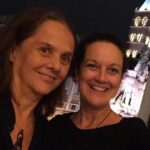 Two women smiling for a picture in front of a building.